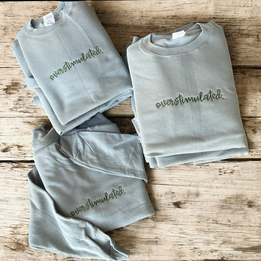 Folded gray sweatshirts with 'ever stimulated.' text on a wooden surface