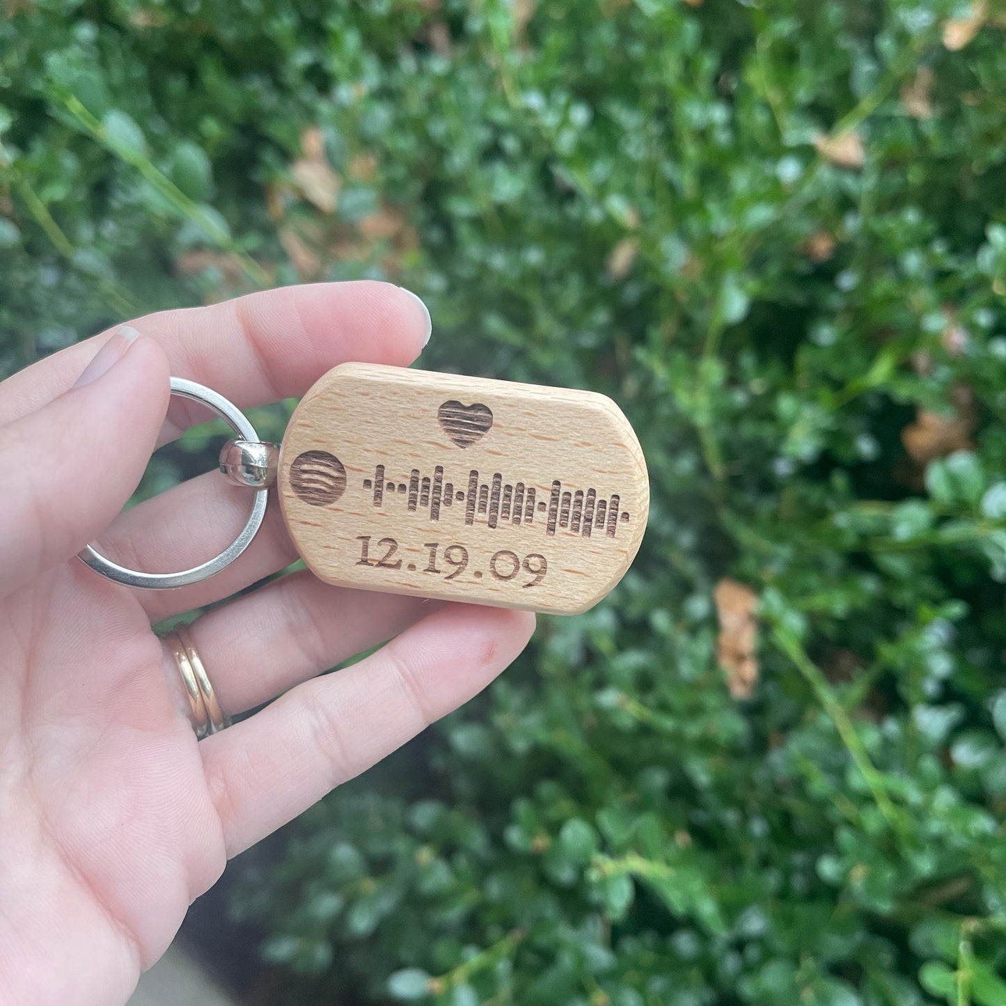 Wooden keychain with engraved date held by a hand against a green leafy background