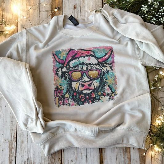 White sweatshirt with a colorful cow design on a wooden surface with Christmas decorations.