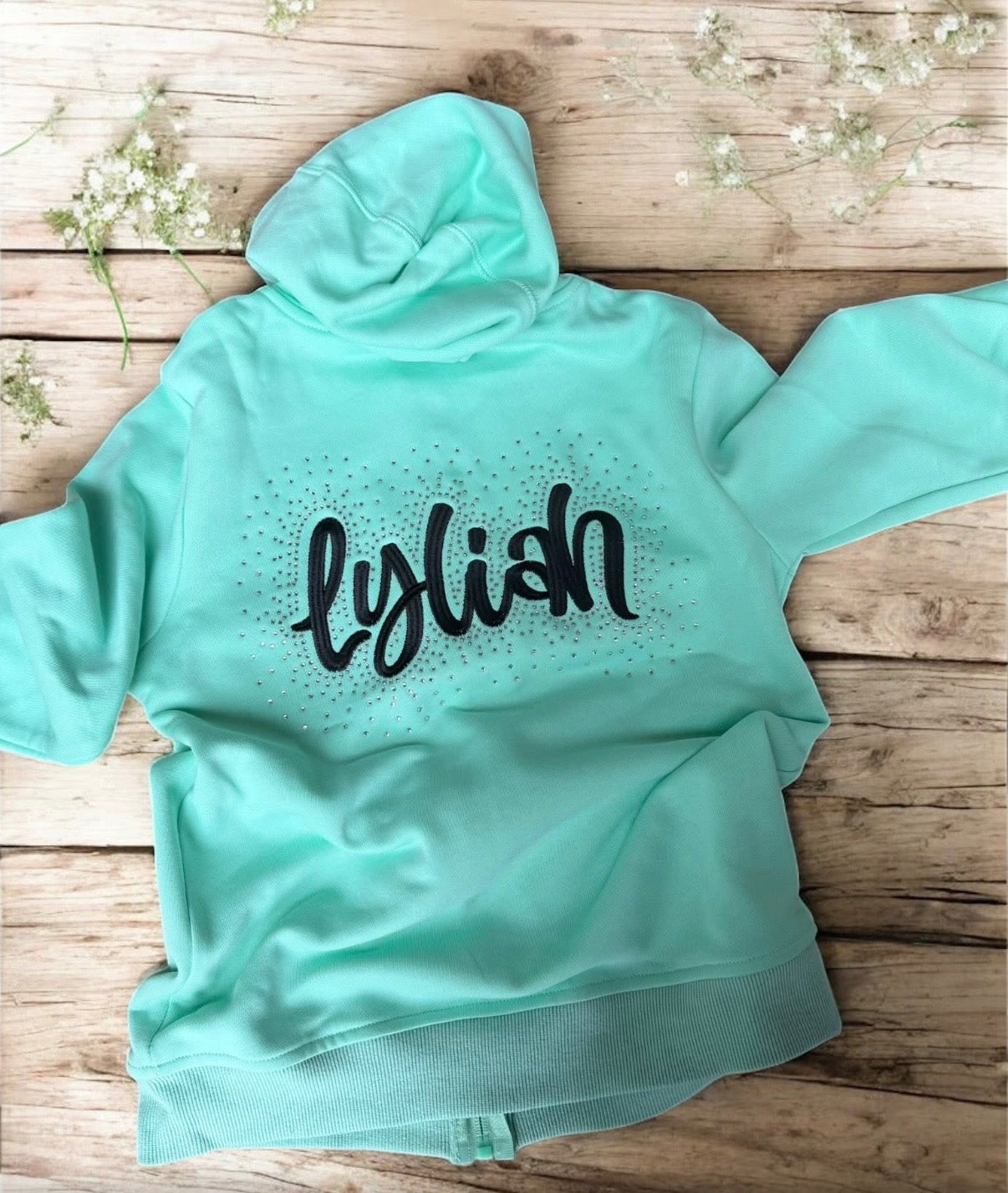 Mint green hoodie with 'lylish' text on a wooden surface