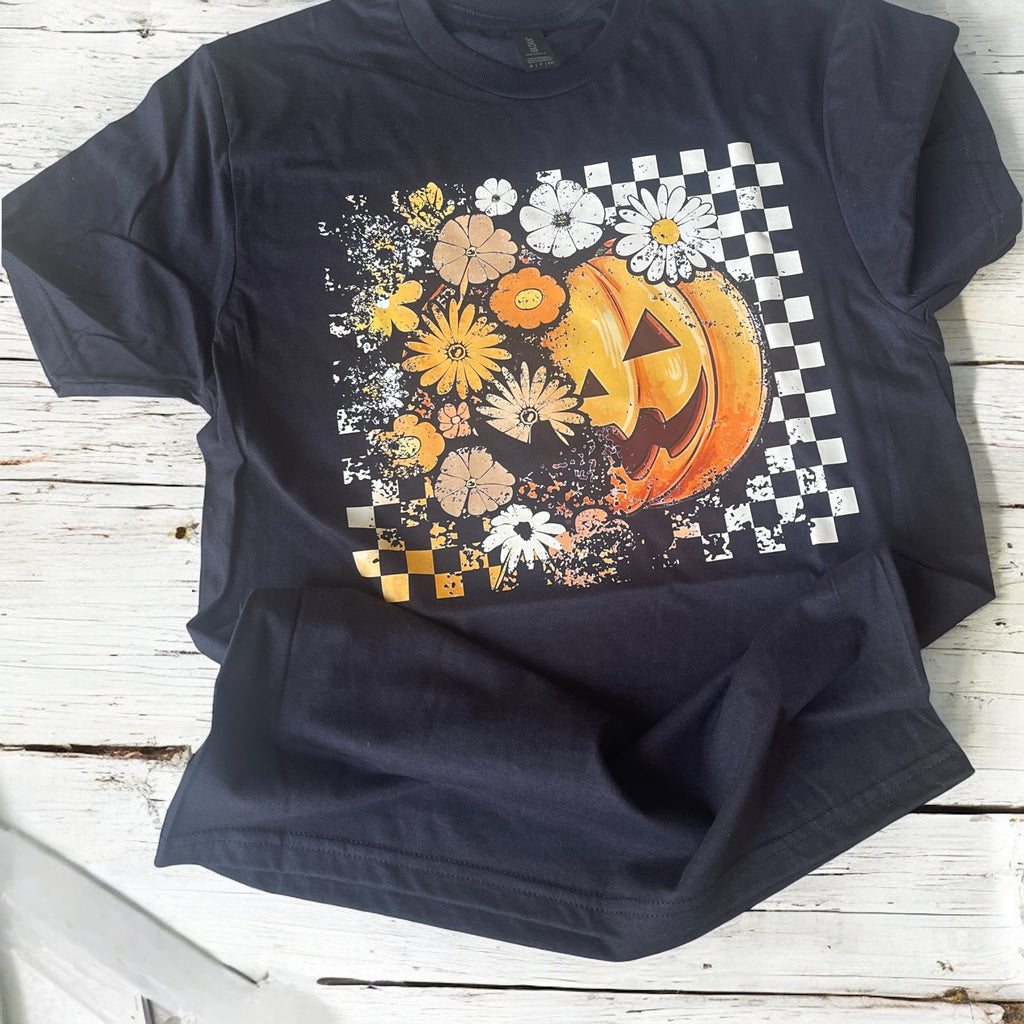 Black t-shirt with a Halloween-themed design featuring a pumpkin and flowers on a checkered background.