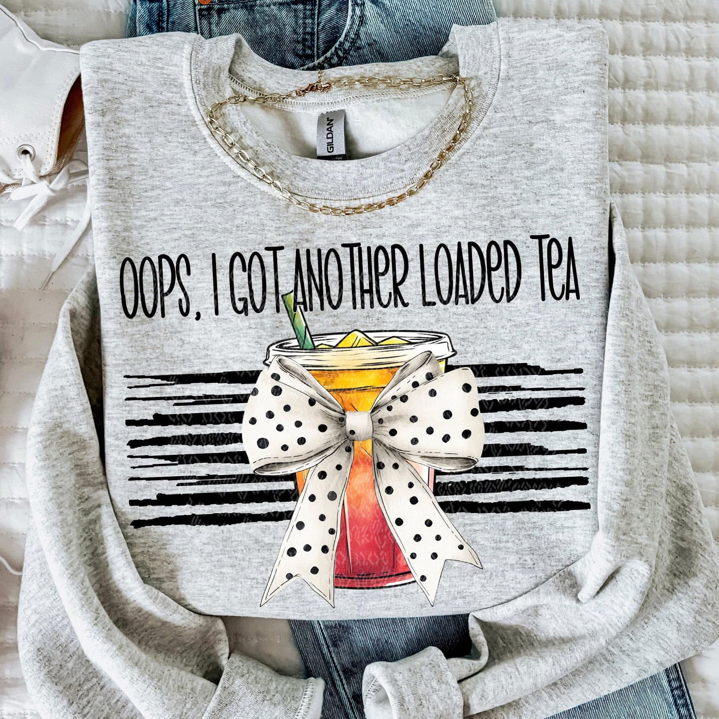 Gray sweatshirt with a graphic design of a cocktail and text 'Oops, I got another loaded tea' on a textured surface.