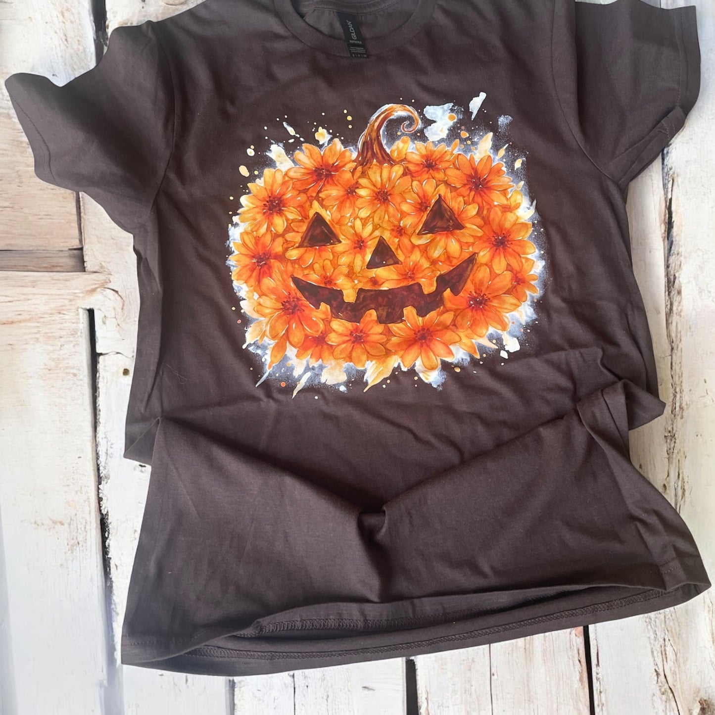 Black t-shirt with a pumpkin design made of flowers on a wooden surface