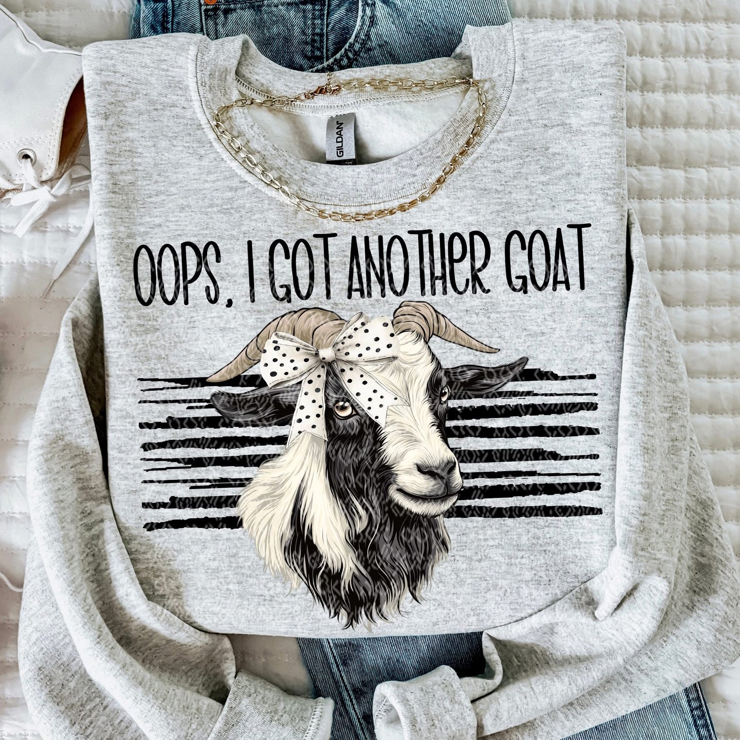 Gray sweatshirt with a graphic of a goat and text 'Oops, I got another goat' on a textured surface.