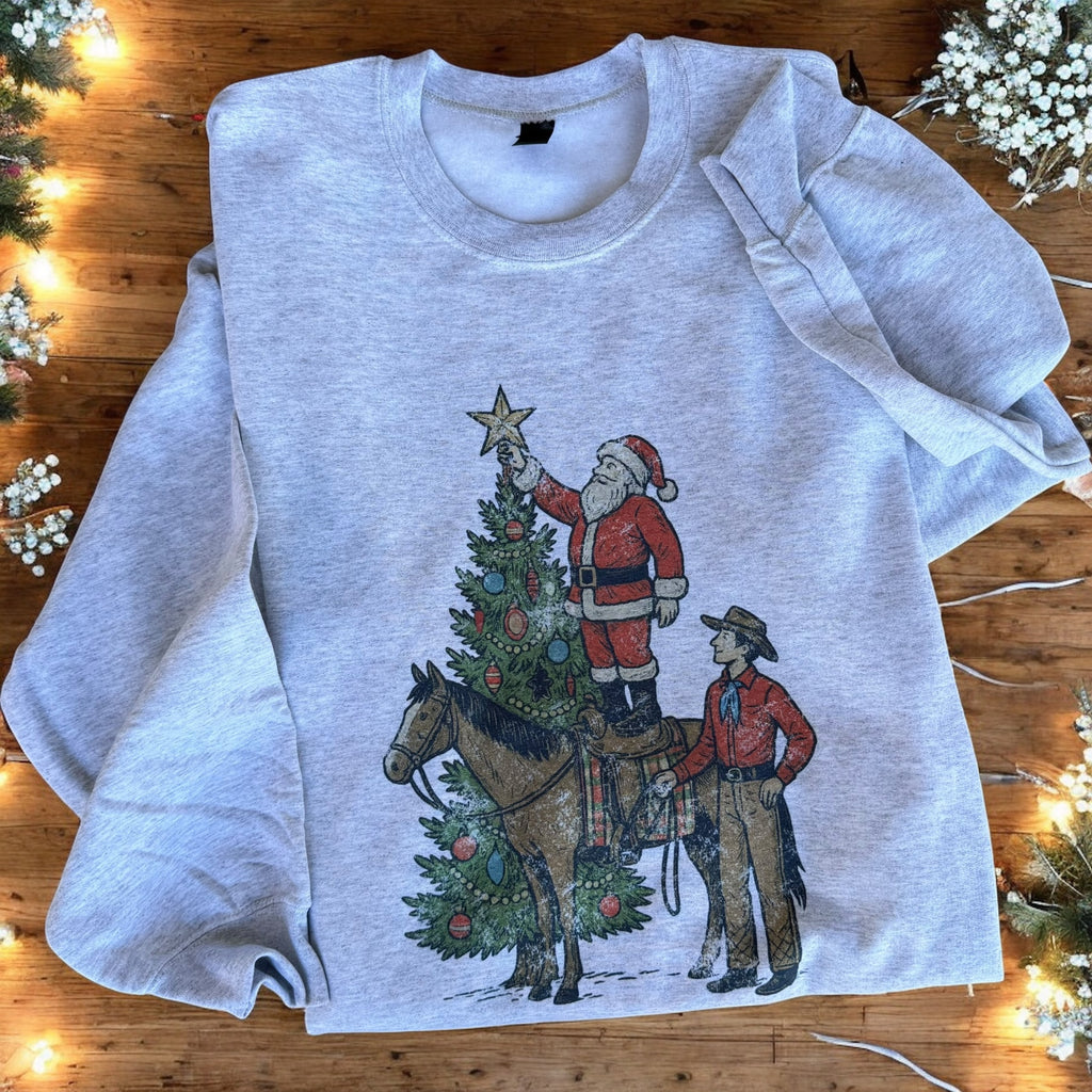 Gray sweatshirt with Santa Claus and a cowboy graphic on a wooden surface with Christmas decorations.