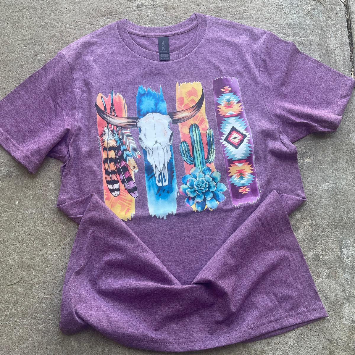 Purple t-shirt with a colorful graphic of a bull skull, cactus, and feathers on a gray surface.