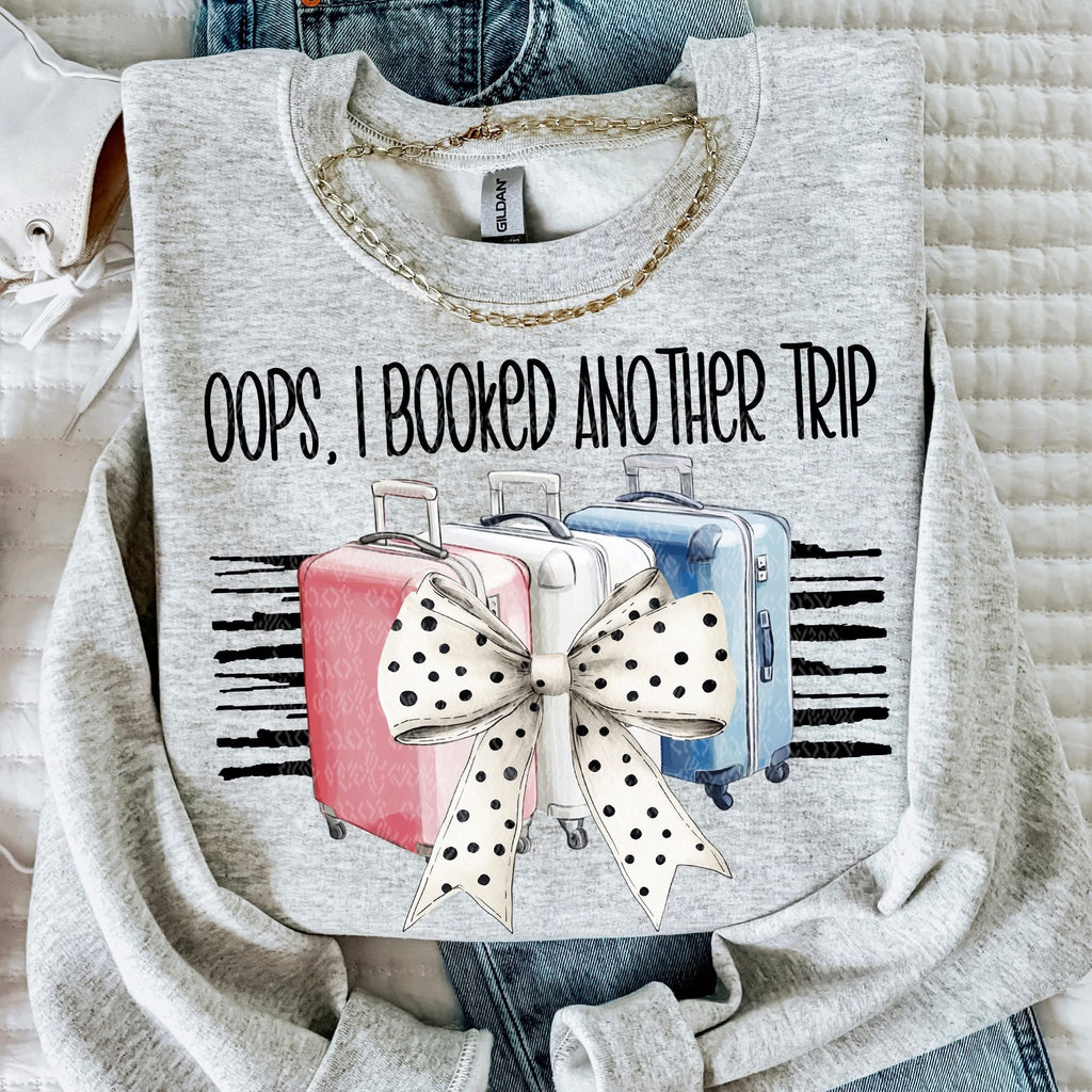 Gray sweatshirt with 'Oops, I Booked Another Trip' text and suitcase design.