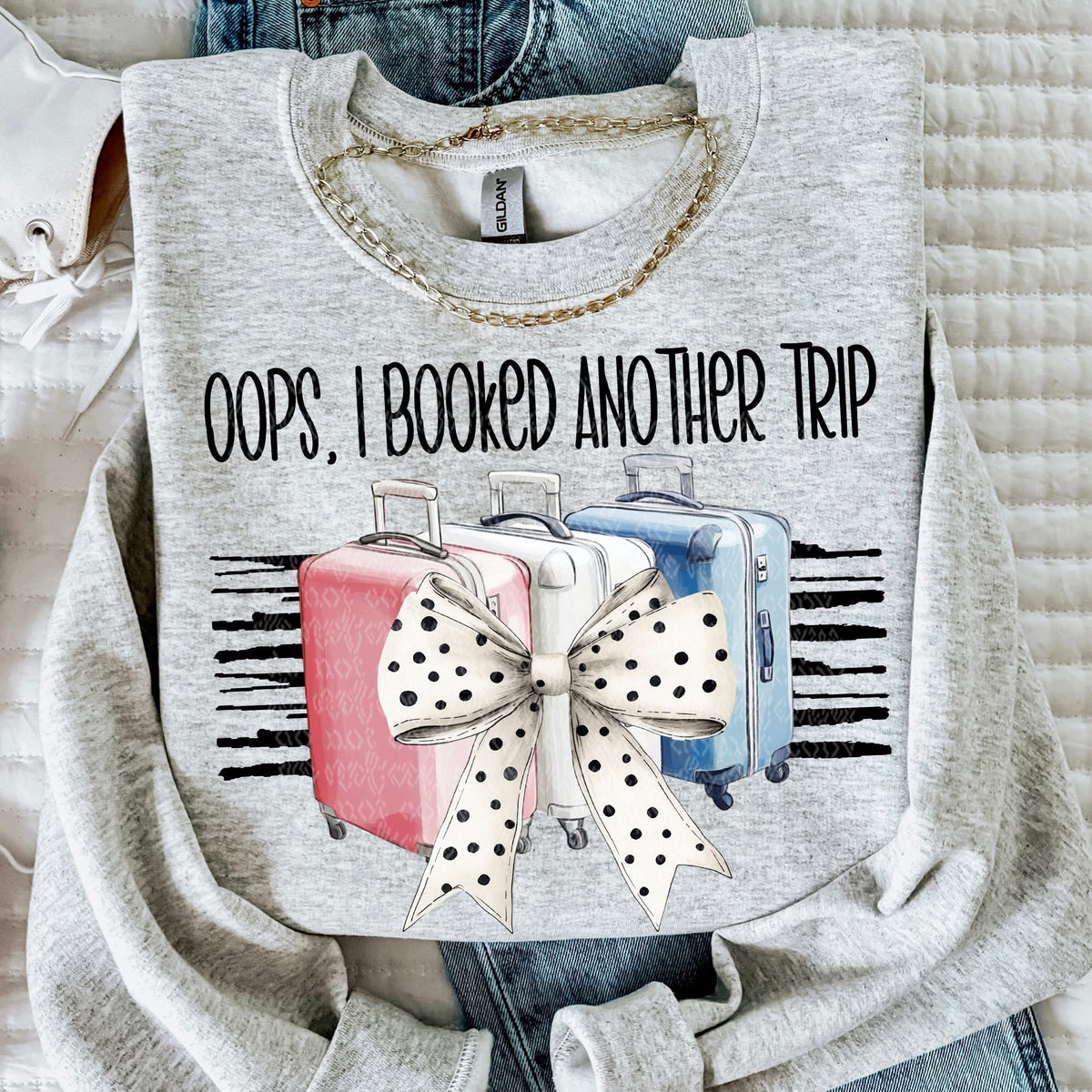 Gray sweatshirt with 'Oops, I Booked Another Trip' text and suitcase design.