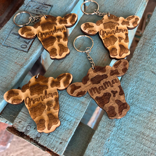 Wooden keychains shaped like hands with engraved names on a rustic wooden surface.