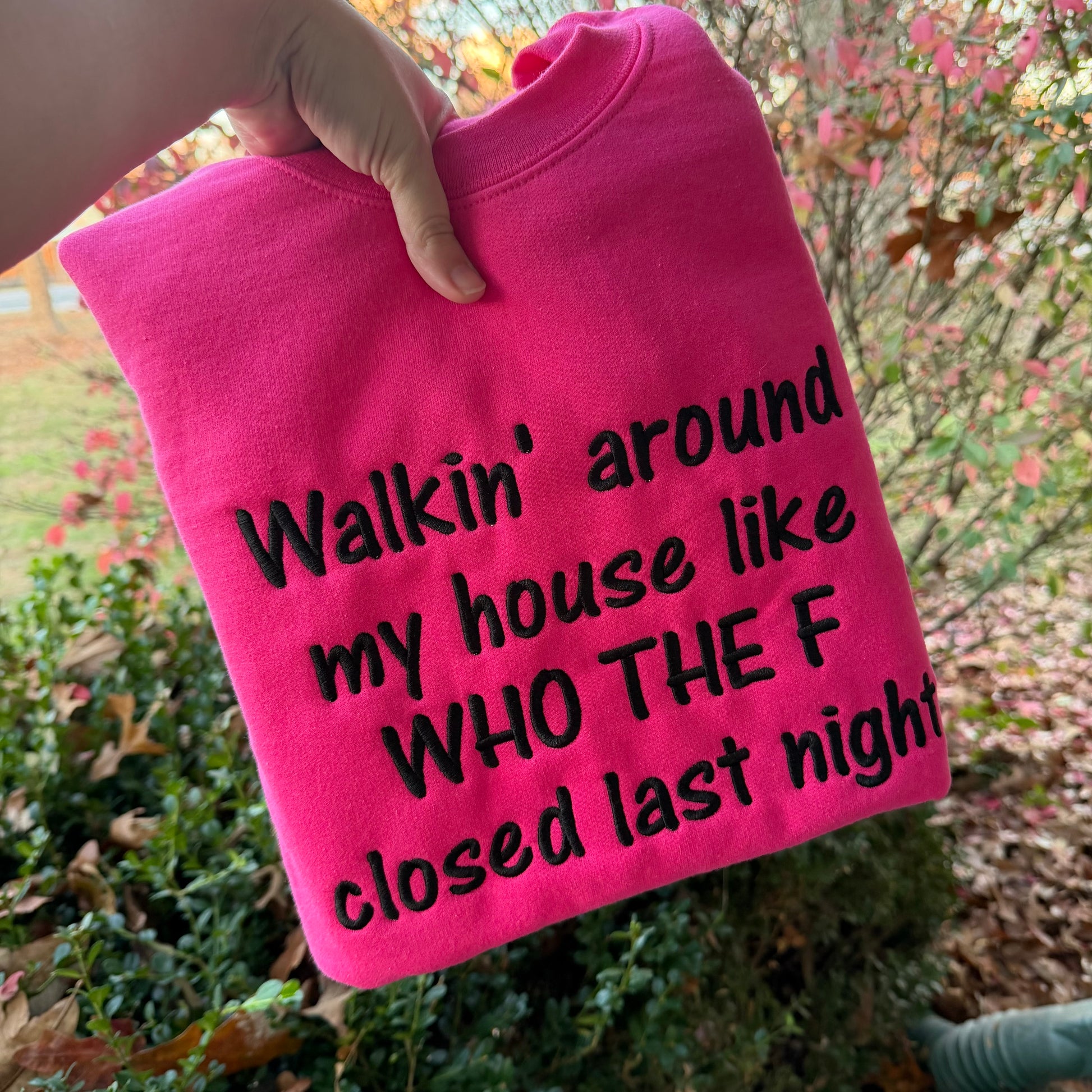 Pink sweatshirt with black text held by a hand outdoors.