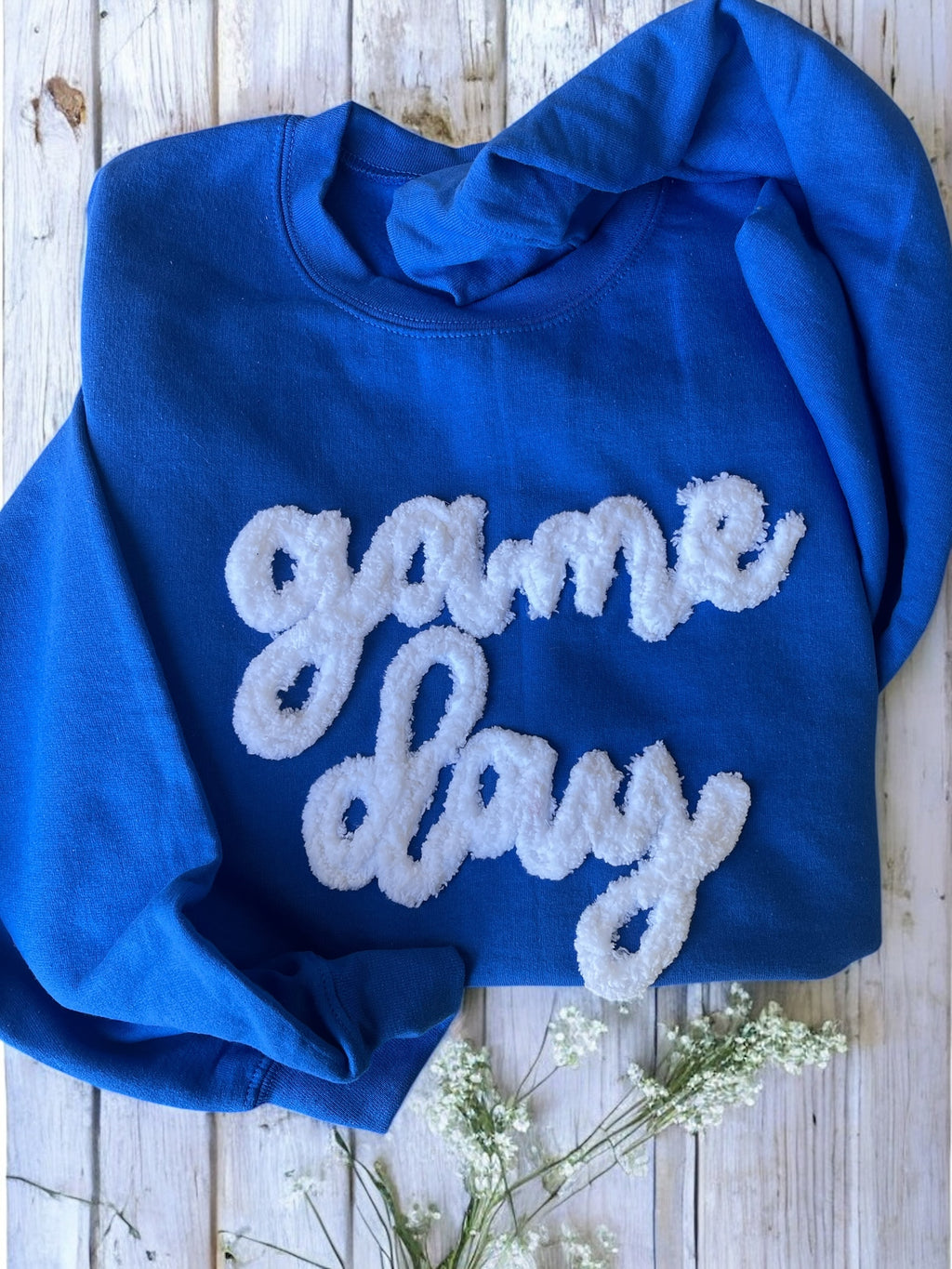 Blue sweatshirt with 'game day' text on a wooden surface with flowers.