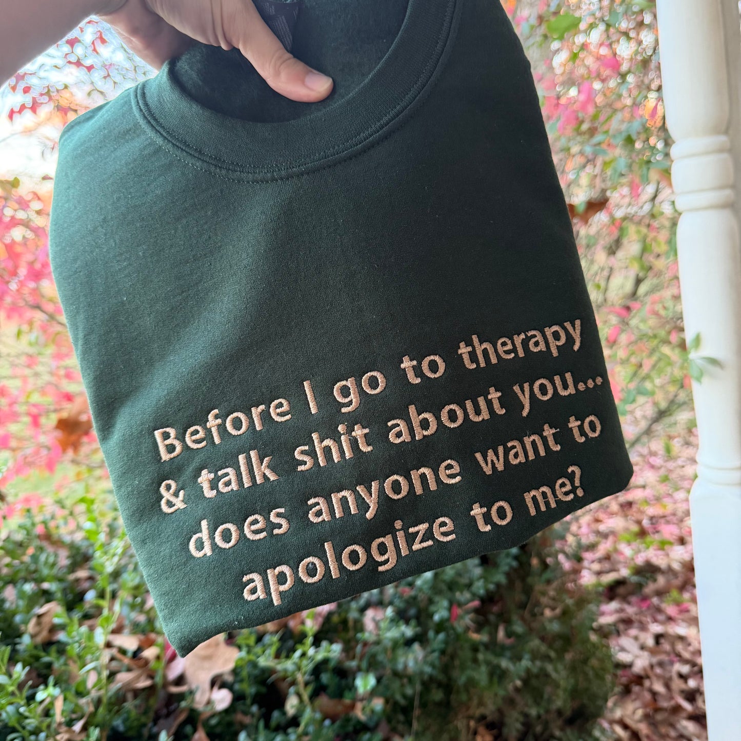 Green sweatshirt with printed text held by a person outdoors.