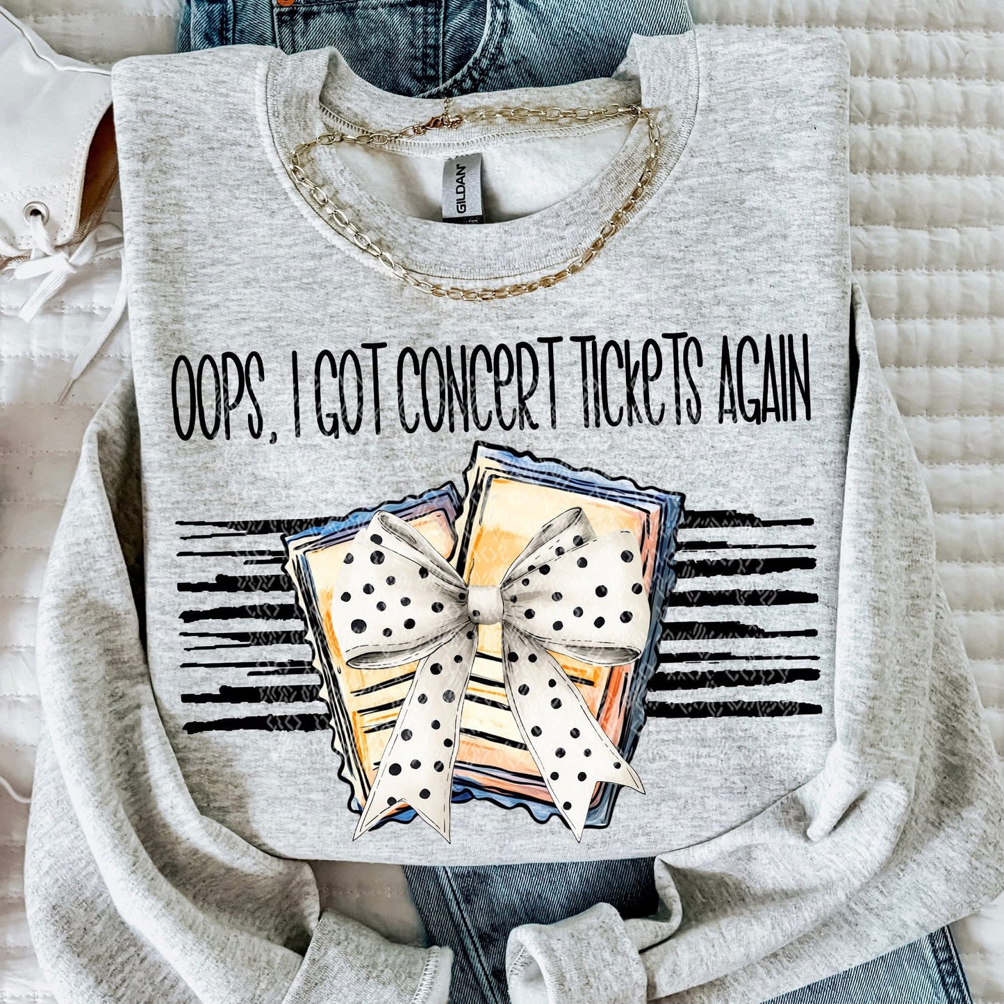 Gray sweatshirt with 'Oops, I Got Concert Tickets Again' text and graphic design on a textured surface.