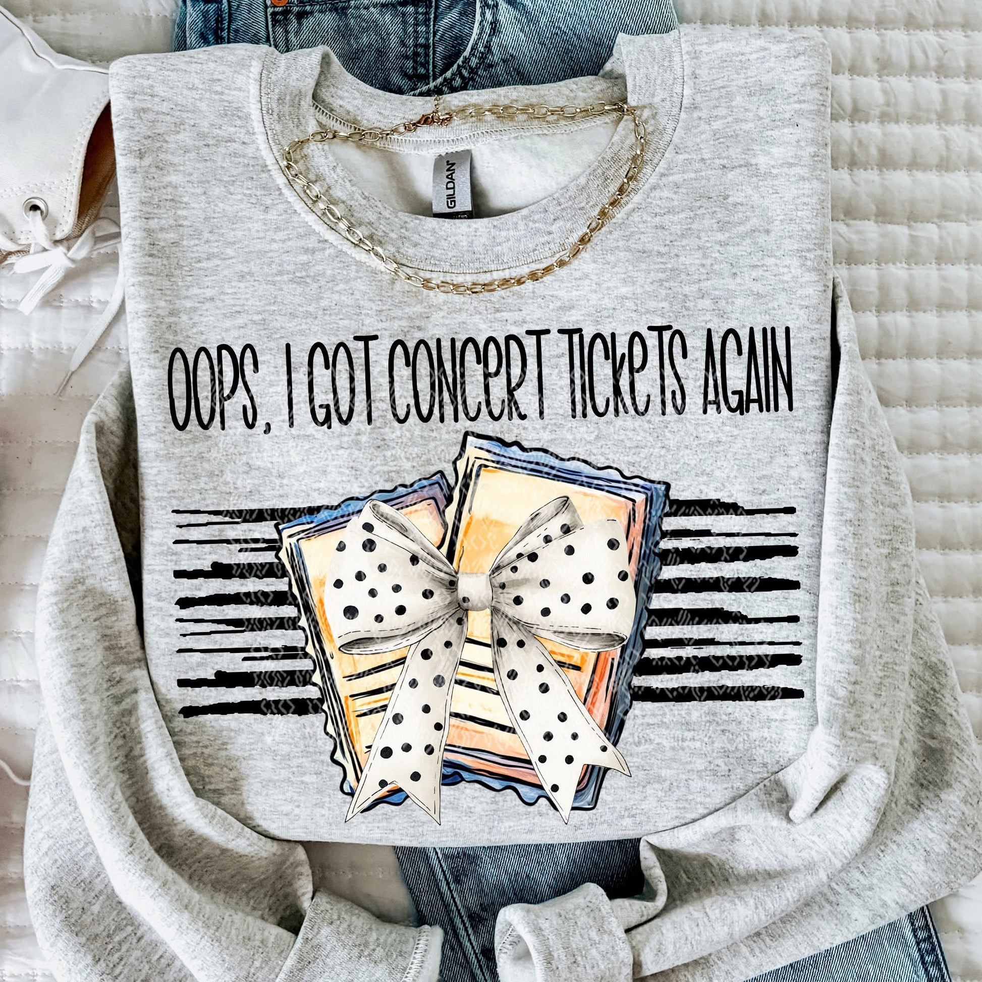 Gray sweatshirt with 'Oops, I Got Concert Tickets Again' text and graphic design on a textured surface.