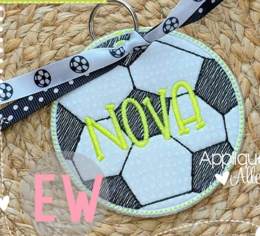 Soccer ball keychain with 'NOVA' embroidered on it, placed on a woven surface.
