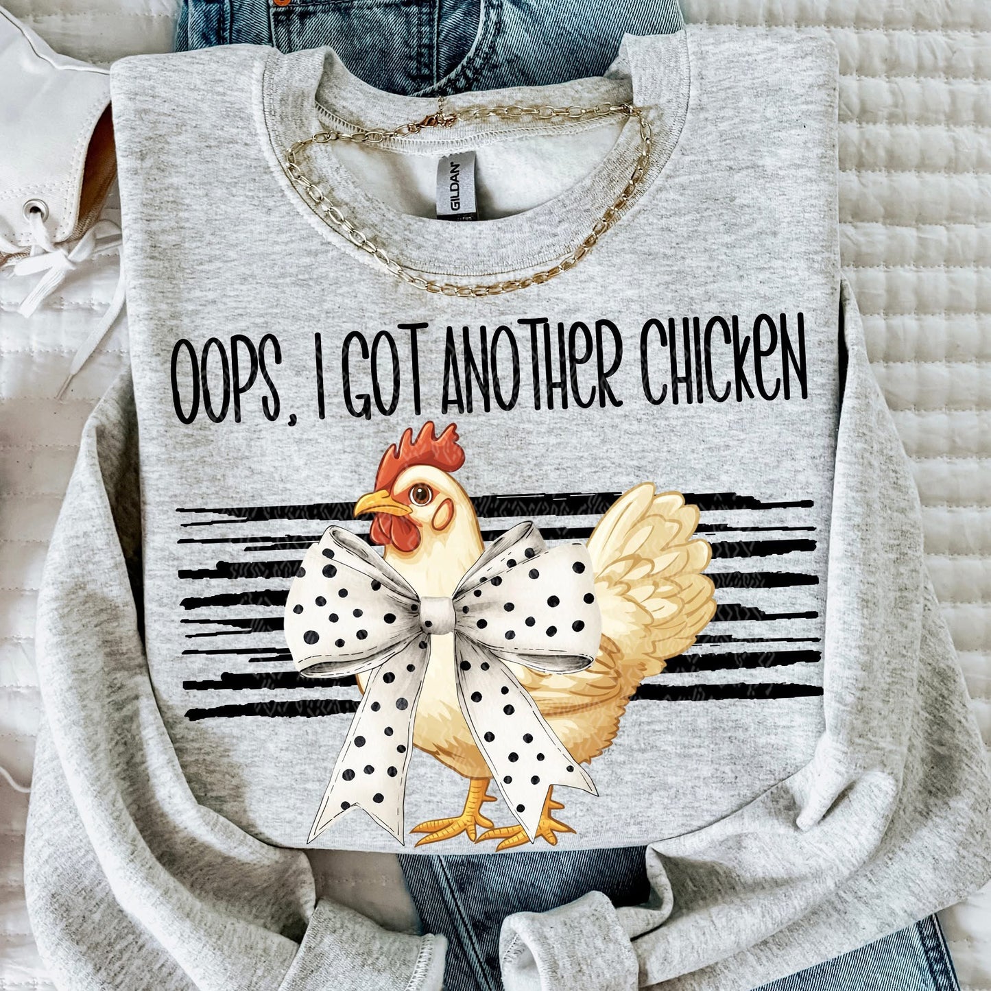 Gray sweatshirt with a chicken graphic and text 'Oops, I got another chicken' on a textured surface.