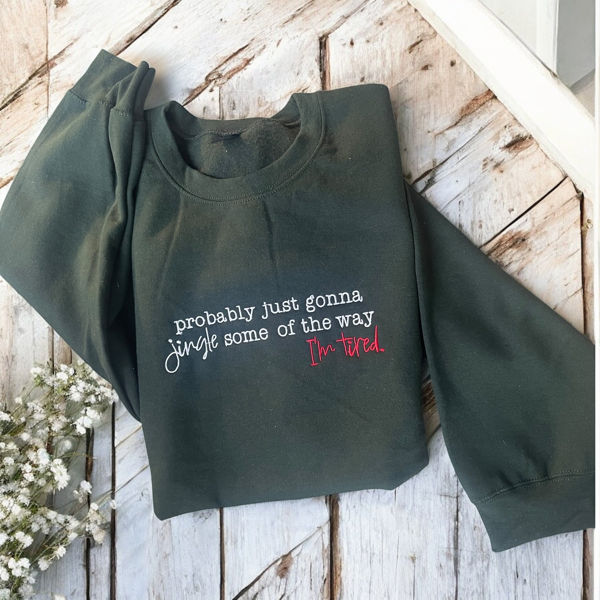 Green sweatshirt with text on a wooden surface with flowers