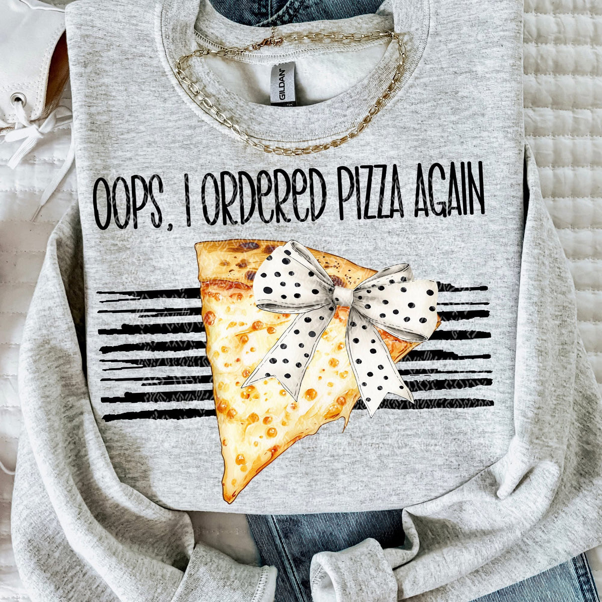 Gray sweatshirt with pizza slice and bow graphic and text 'Oops, I ordered pizza again' on a soft fabric background.