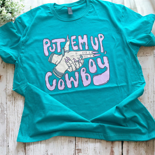 Teal t-shirt with 'Put 'em up, Cowboy' graphic on a wooden surface