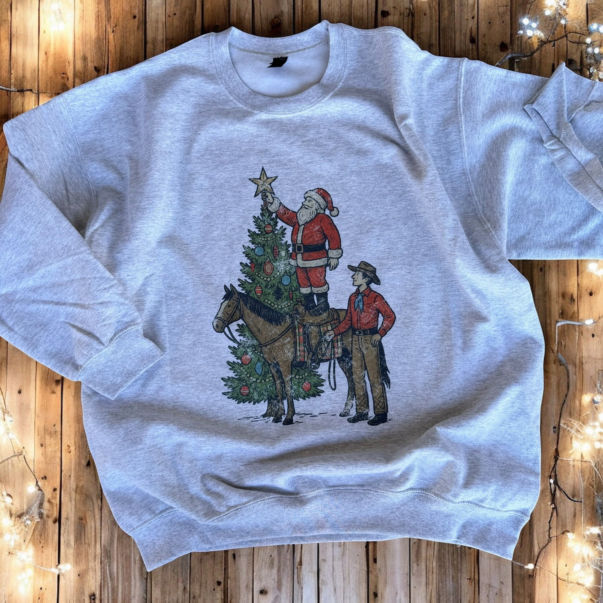 Gray sweatshirt with a Christmas design of Santa and a horse on a wooden surface.