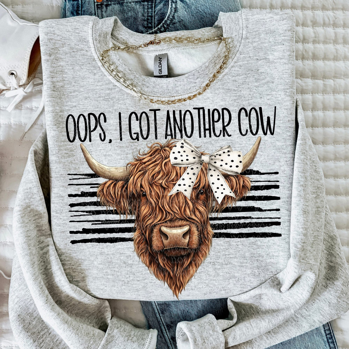 Gray sweatshirt with a cow graphic and text 'Oops, I got another cow' on a textured surface.