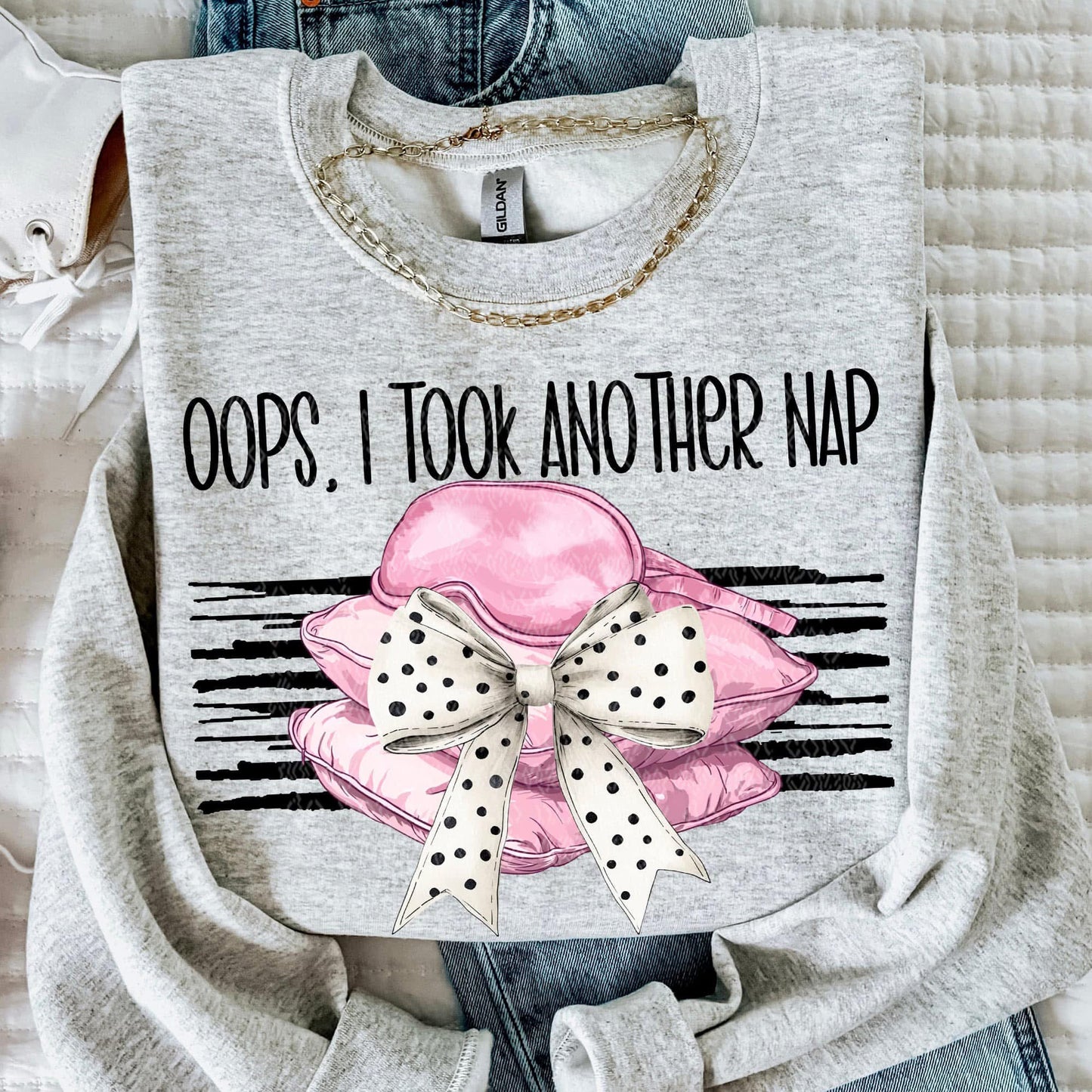 Gray sweatshirt with pink pillow and polka dot bow graphic and text 'Oops, I took another nap' on a textured surface.
