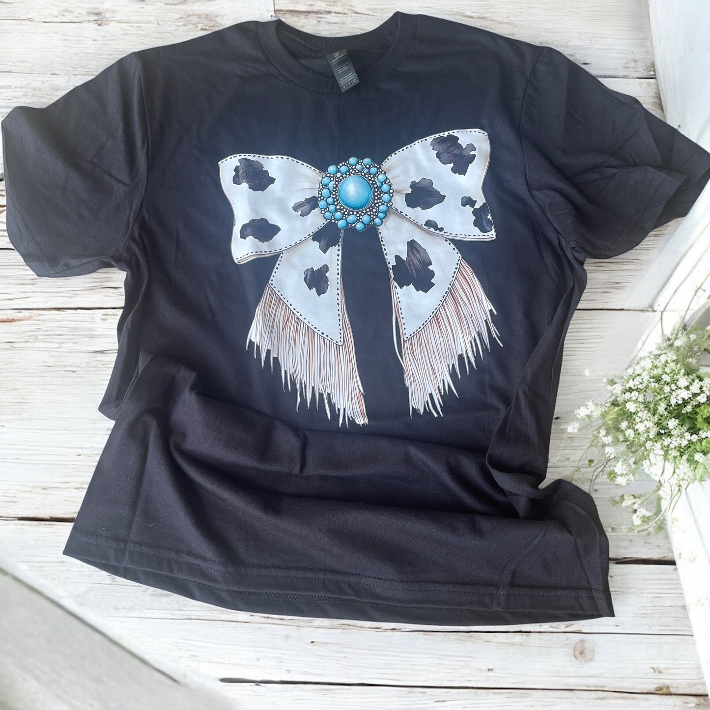 Black t-shirt with a decorative bow design on a wooden surface