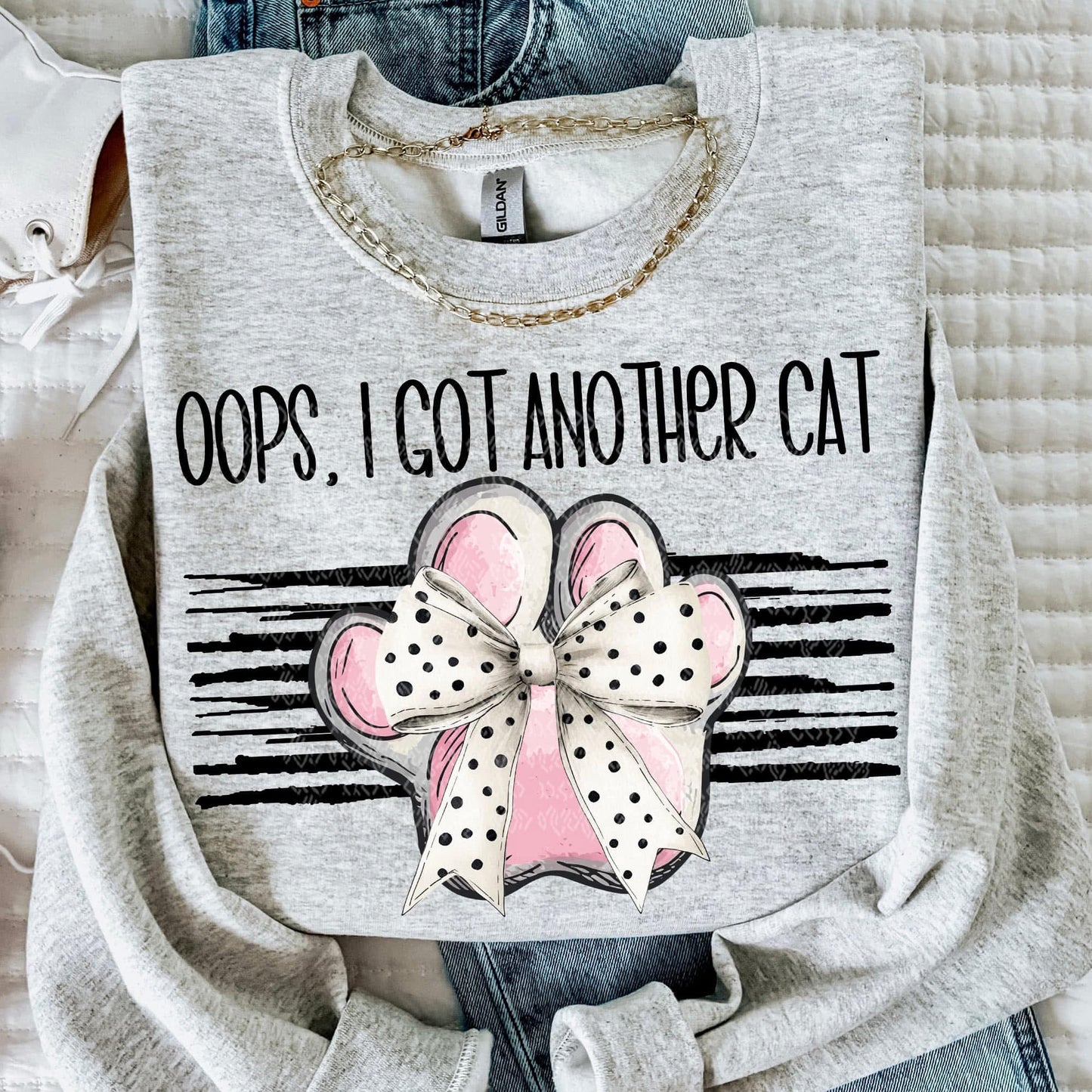 Gray sweatshirt with a pink bow graphic and text 'Oops, I Got Another Cat' on a textured surface.