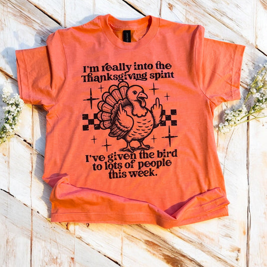 Orange t-shirt with a turkey graphic and humorous text on a wooden surface.
