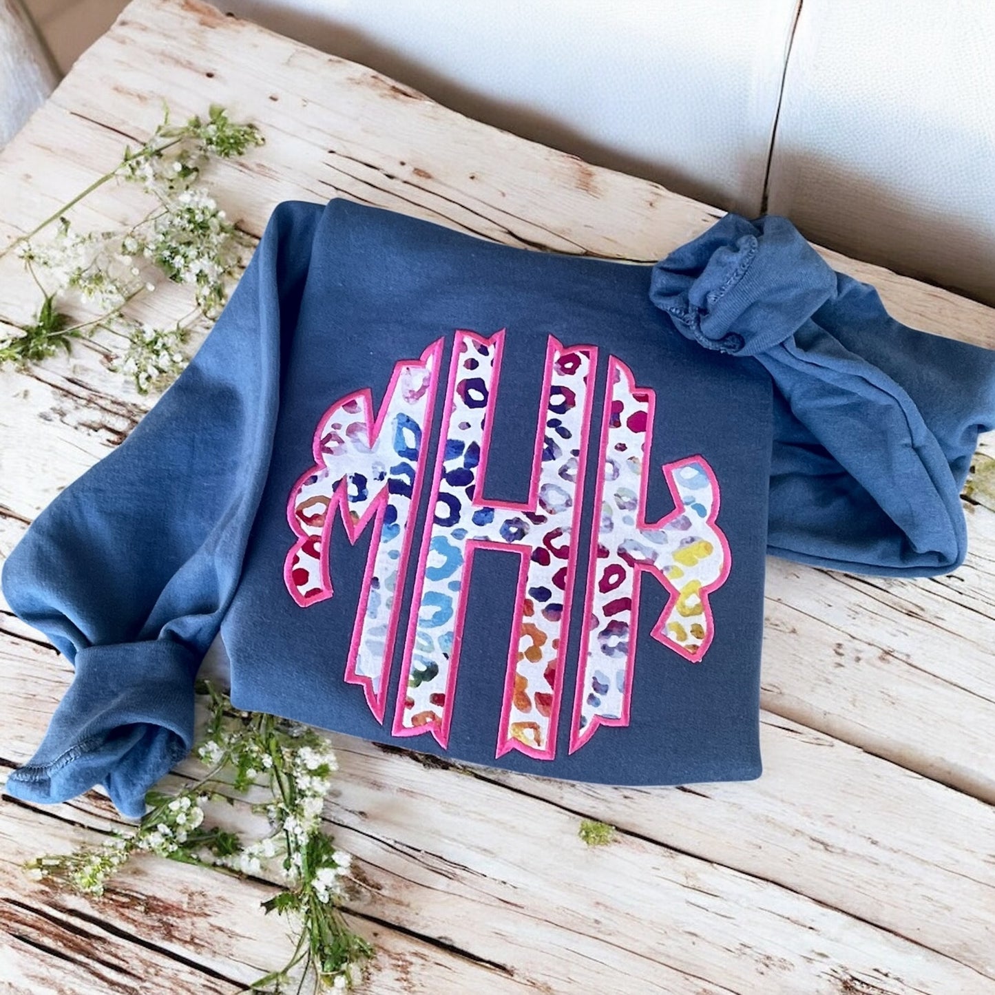 Blue sweatshirt with colorful 'HI' design on a wooden surface