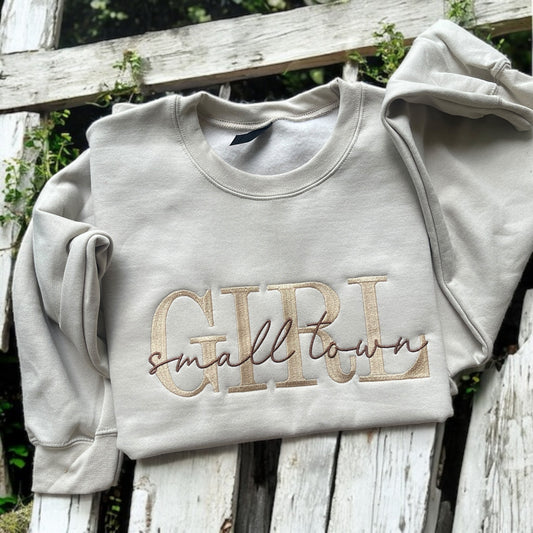 Gray sweatshirt with 'GIRL small town' text on a wooden surface