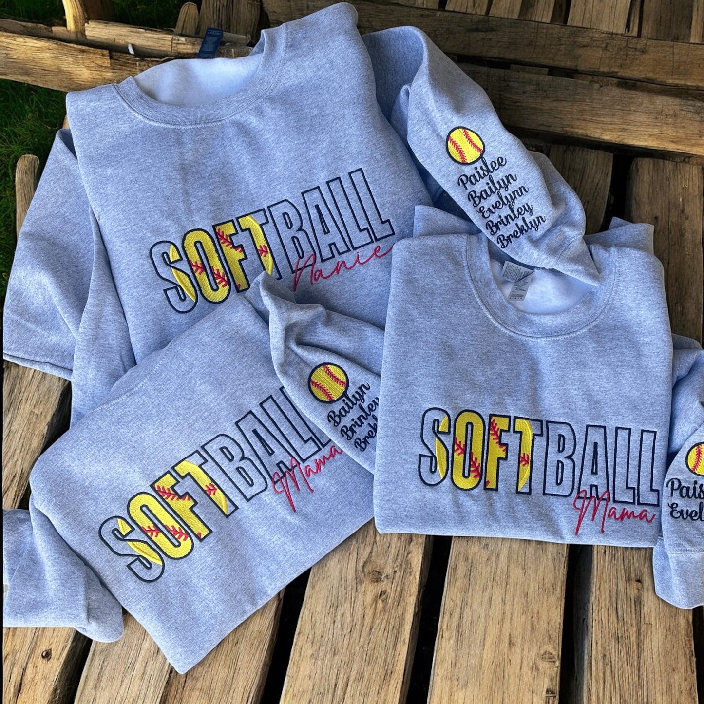 Gray sweatshirts with 'SOFTBALL Mama' text on a wooden surface