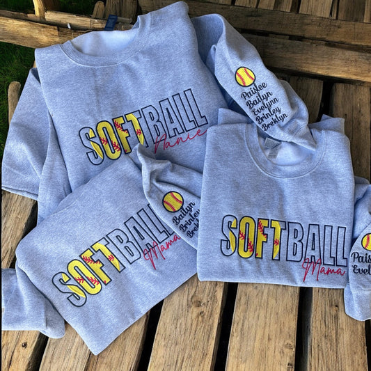 Gray sweatshirts with 'SOFTBALL Mama' text on a wooden surface