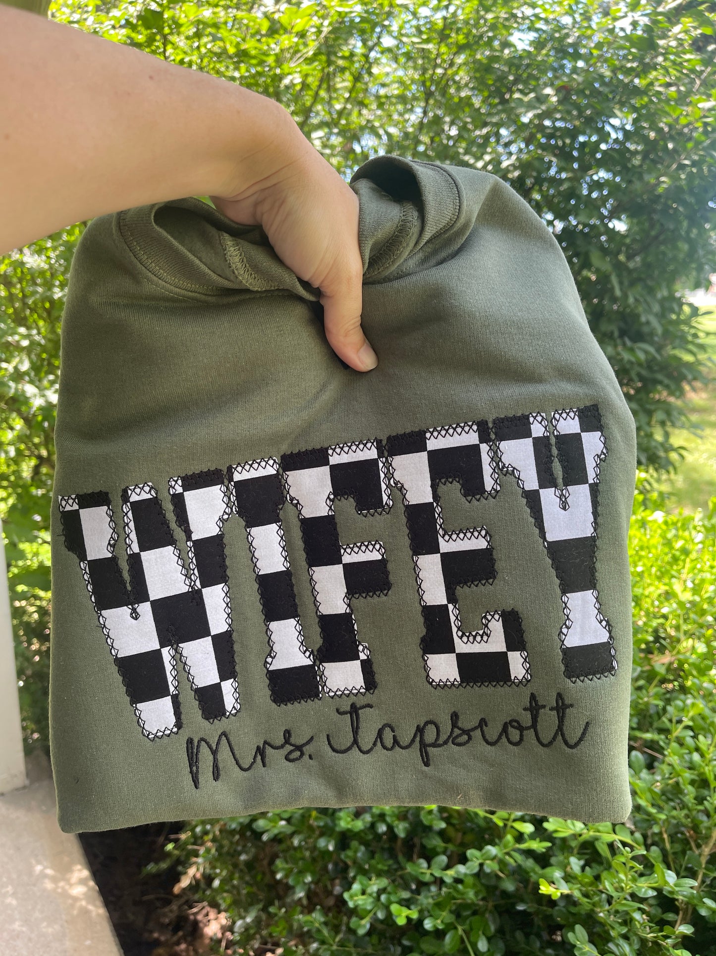 Green shirt with checkered pattern and text held by a hand against a blurred green background