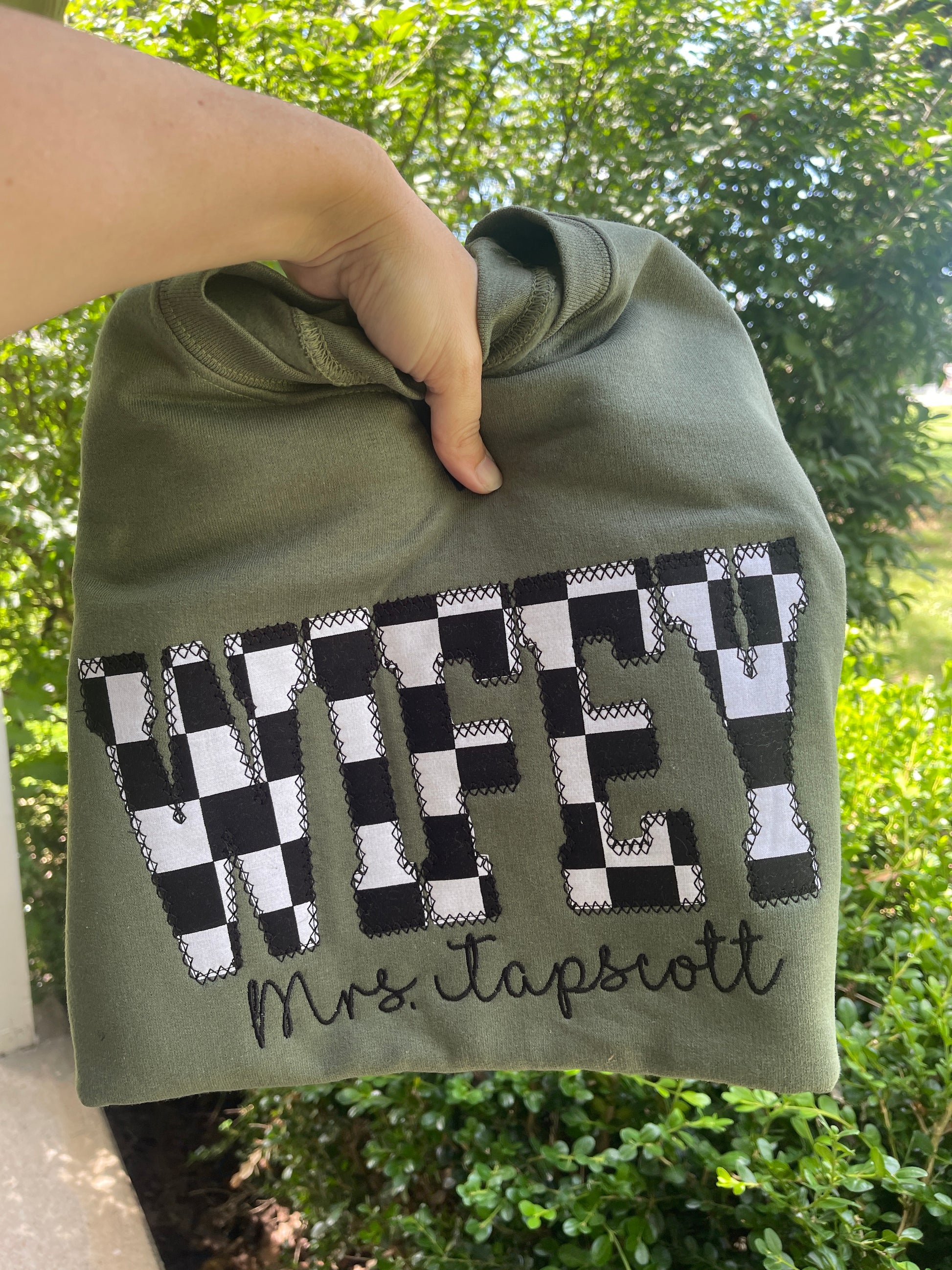 Green shirt with checkered pattern and text held by a hand against a blurred green background