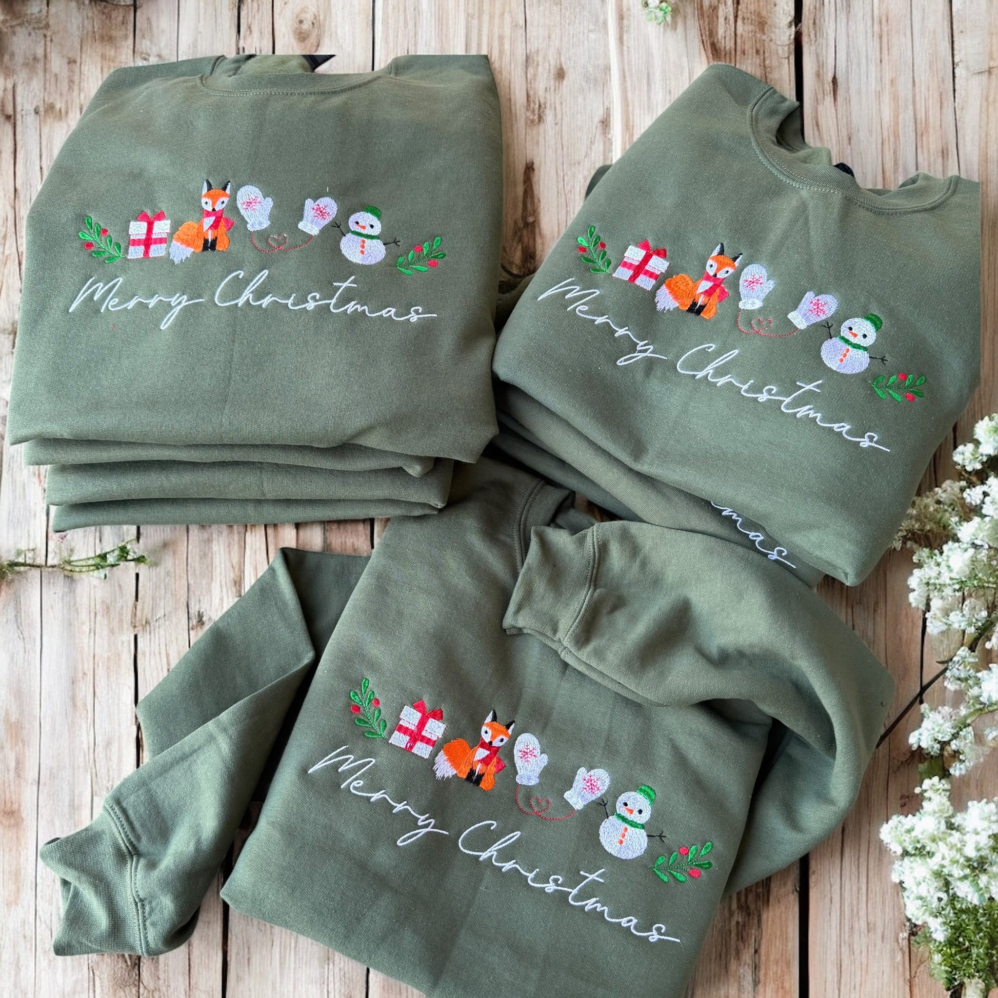Three green sweatshirts with Christmas designs on a wooden surface.