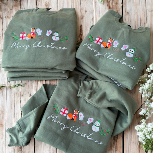 Three green sweatshirts with Christmas designs on a wooden surface.