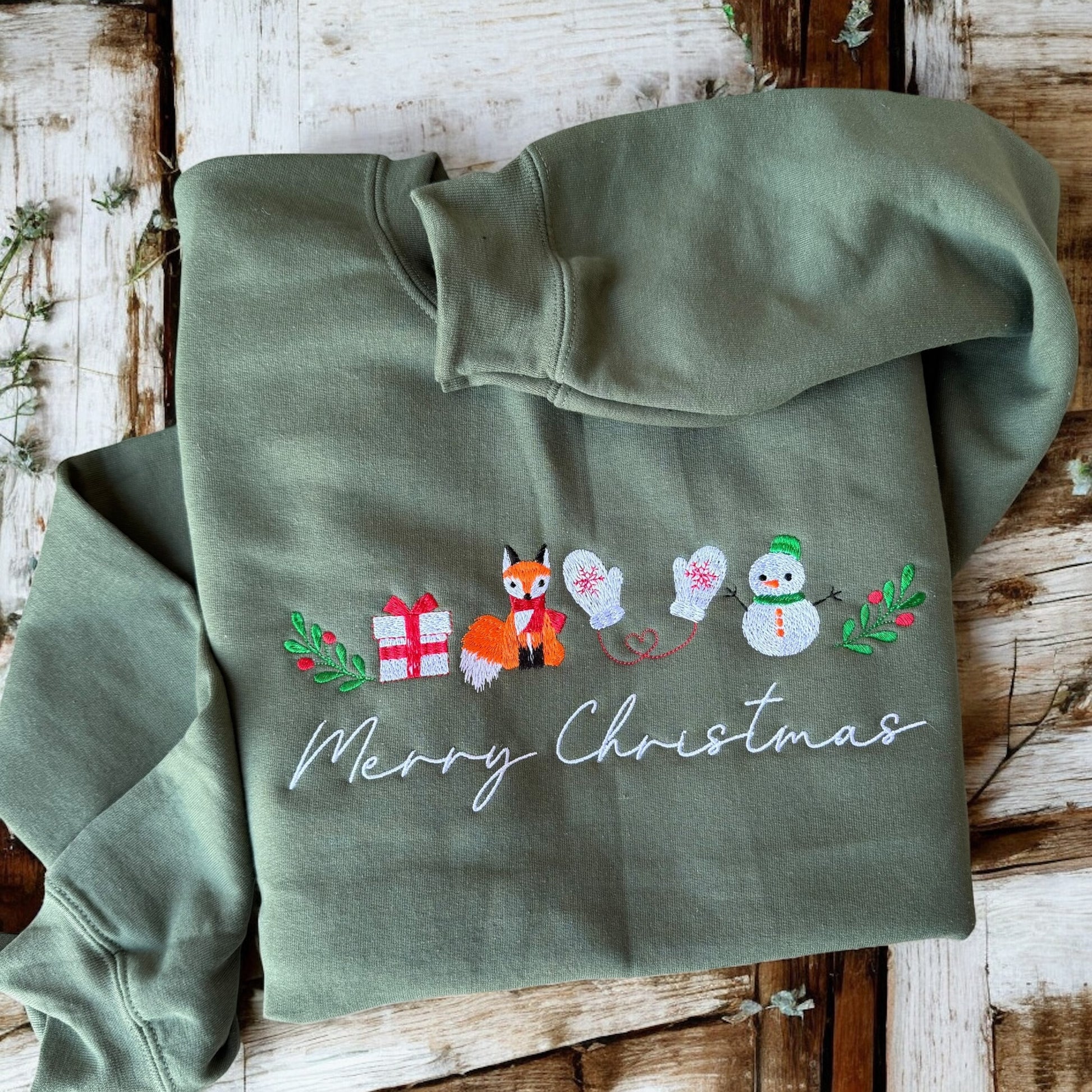 Green hoodie with Christmas-themed embroidery on a wooden surface