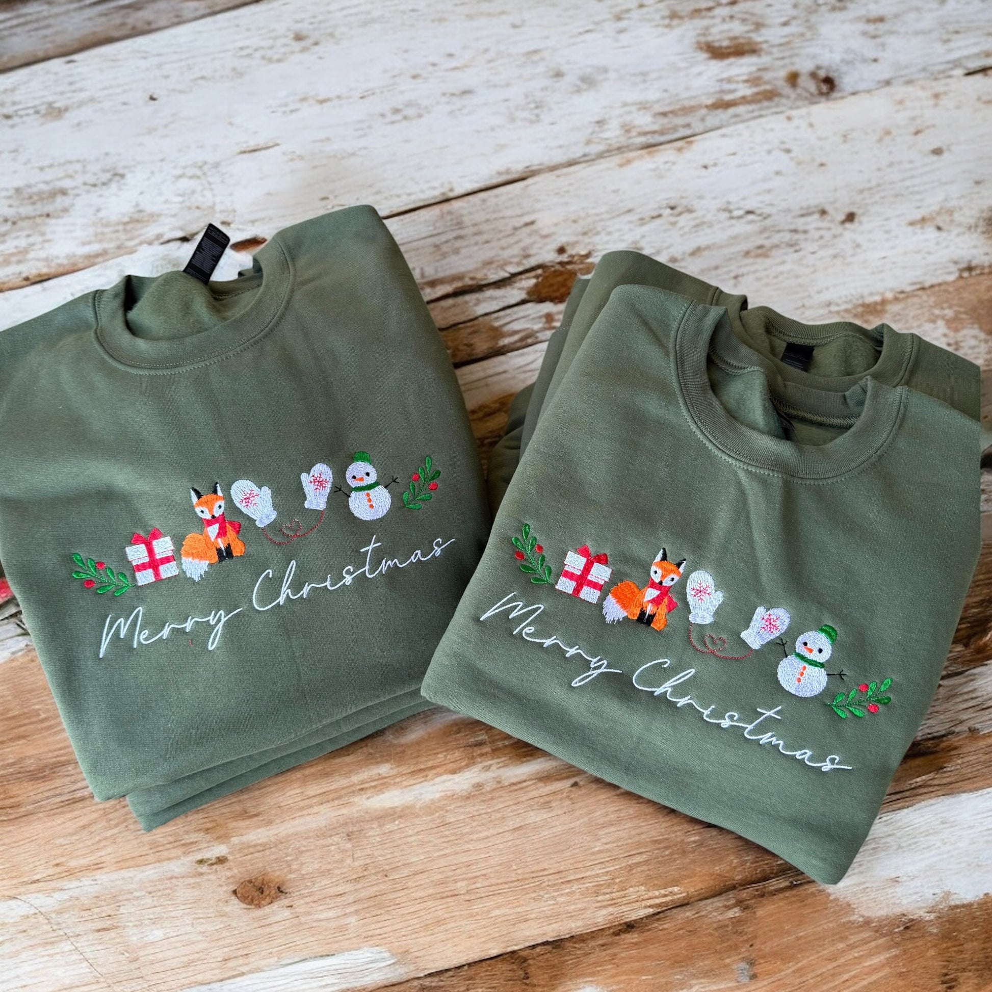 Two green sweatshirts with Christmas designs on a wooden surface