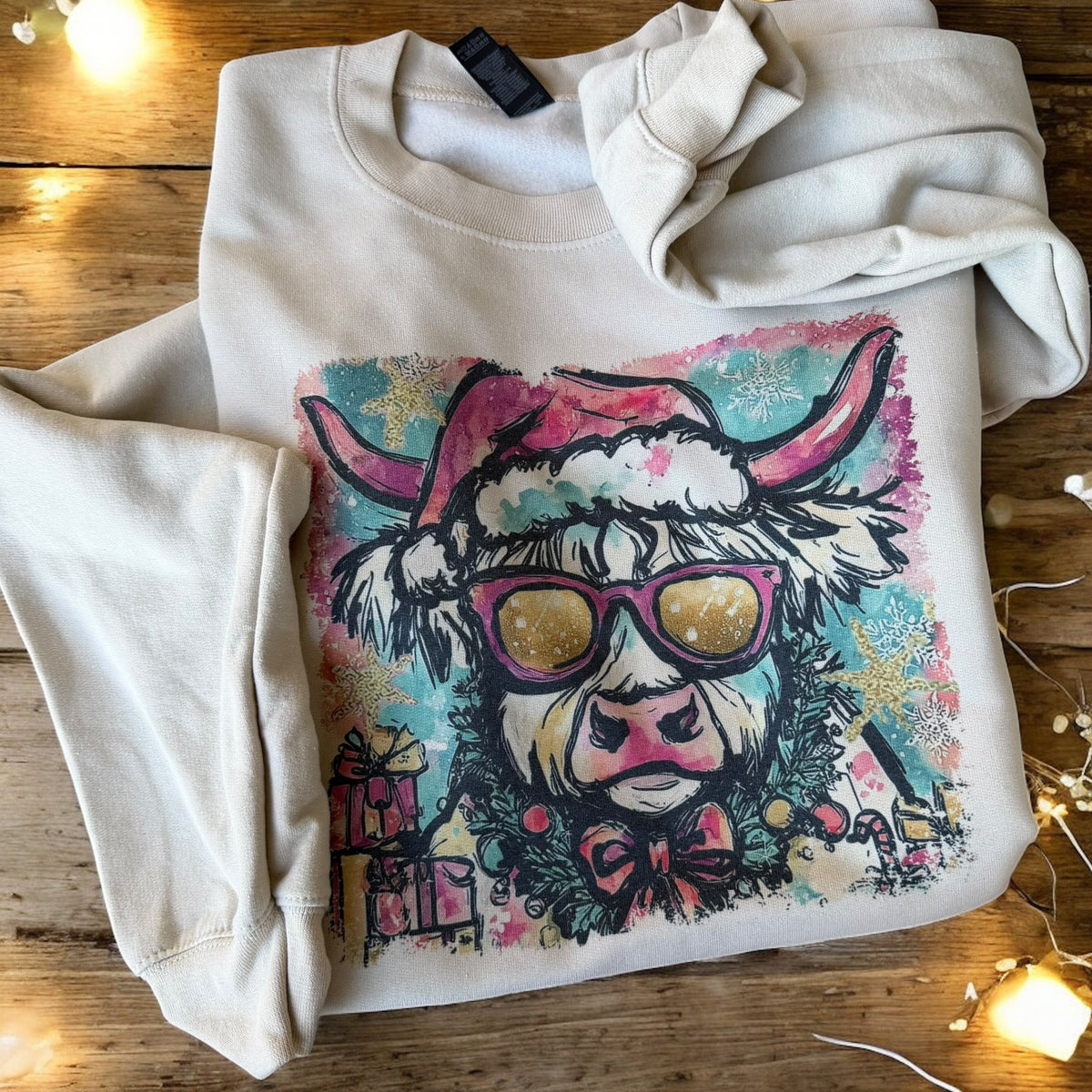 Folded hoodie with a colorful cow design wearing sunglasses on a wooden surface.