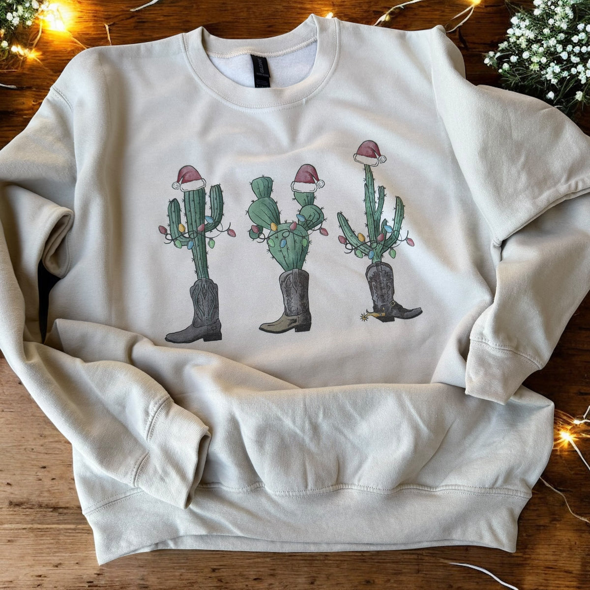 White sweatshirt with Christmas-themed cactus design on a wooden surface.
