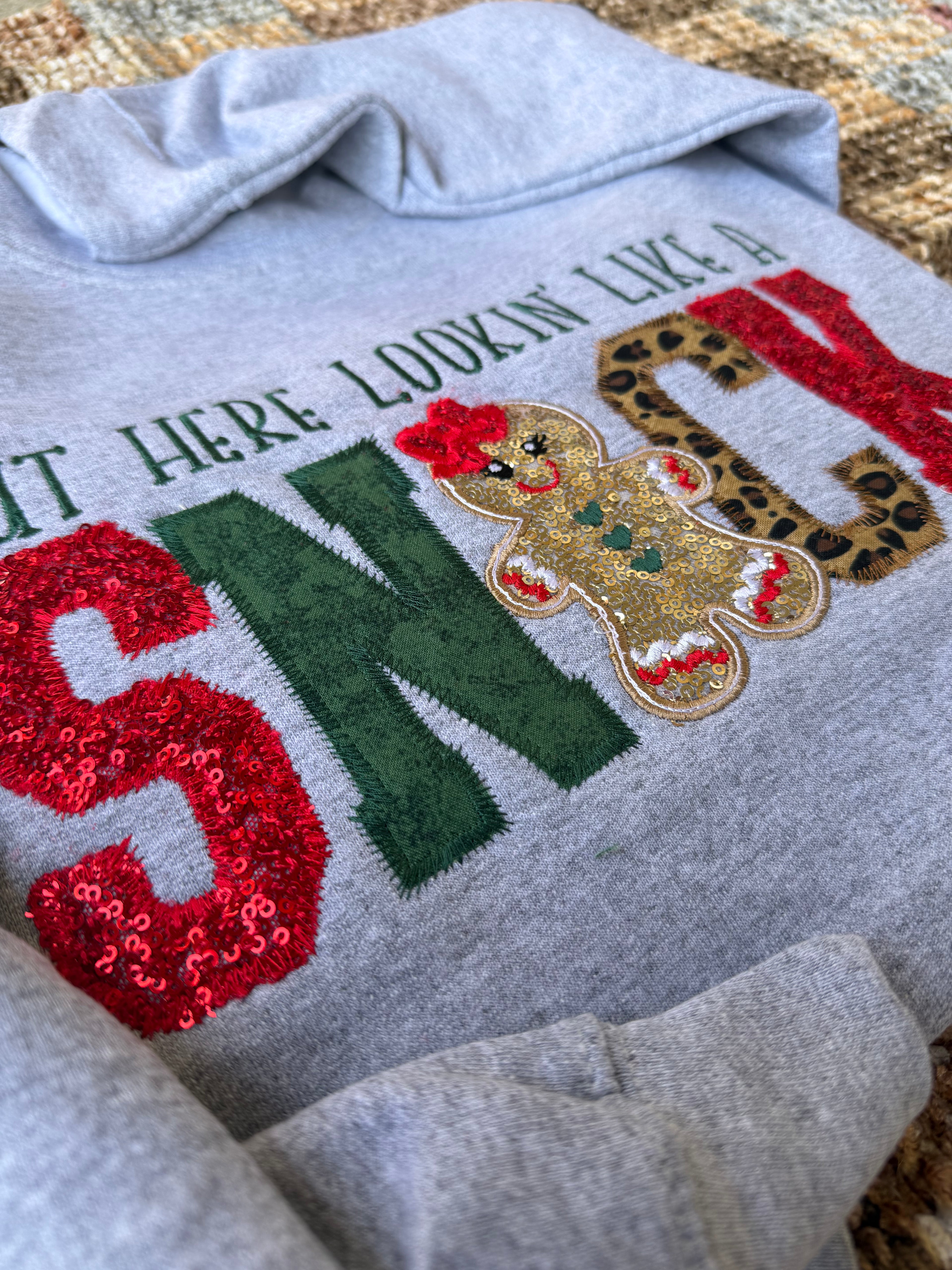 Gray sweatshirt with festive text and gingerbread man design on a textured surface