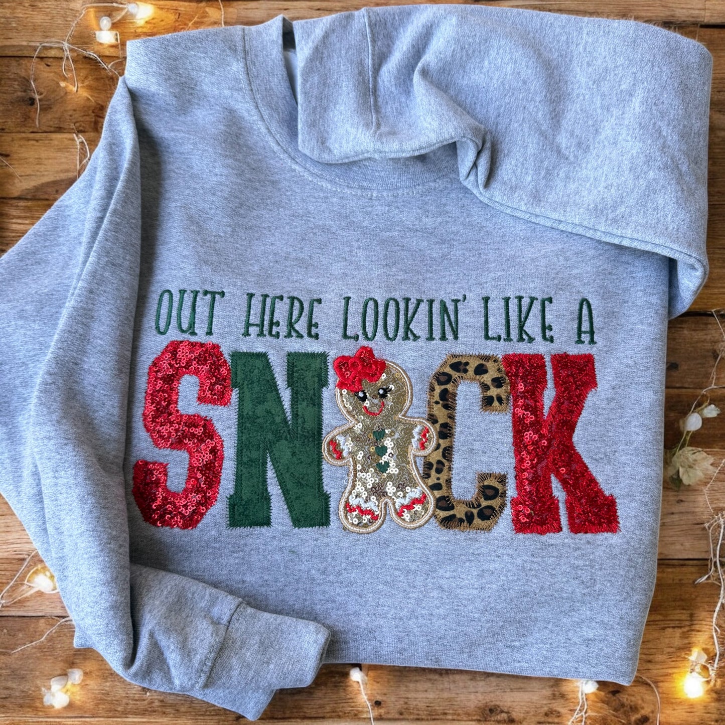 Gray hoodie with festive text and gingerbread design on a wooden surface