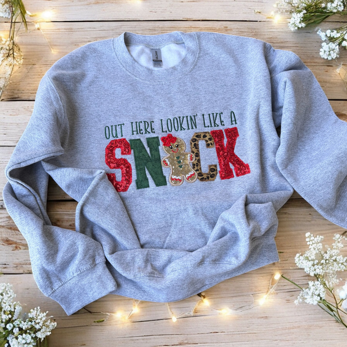 Gray sweatshirt with colorful text on a wooden surface with flowers and lights.