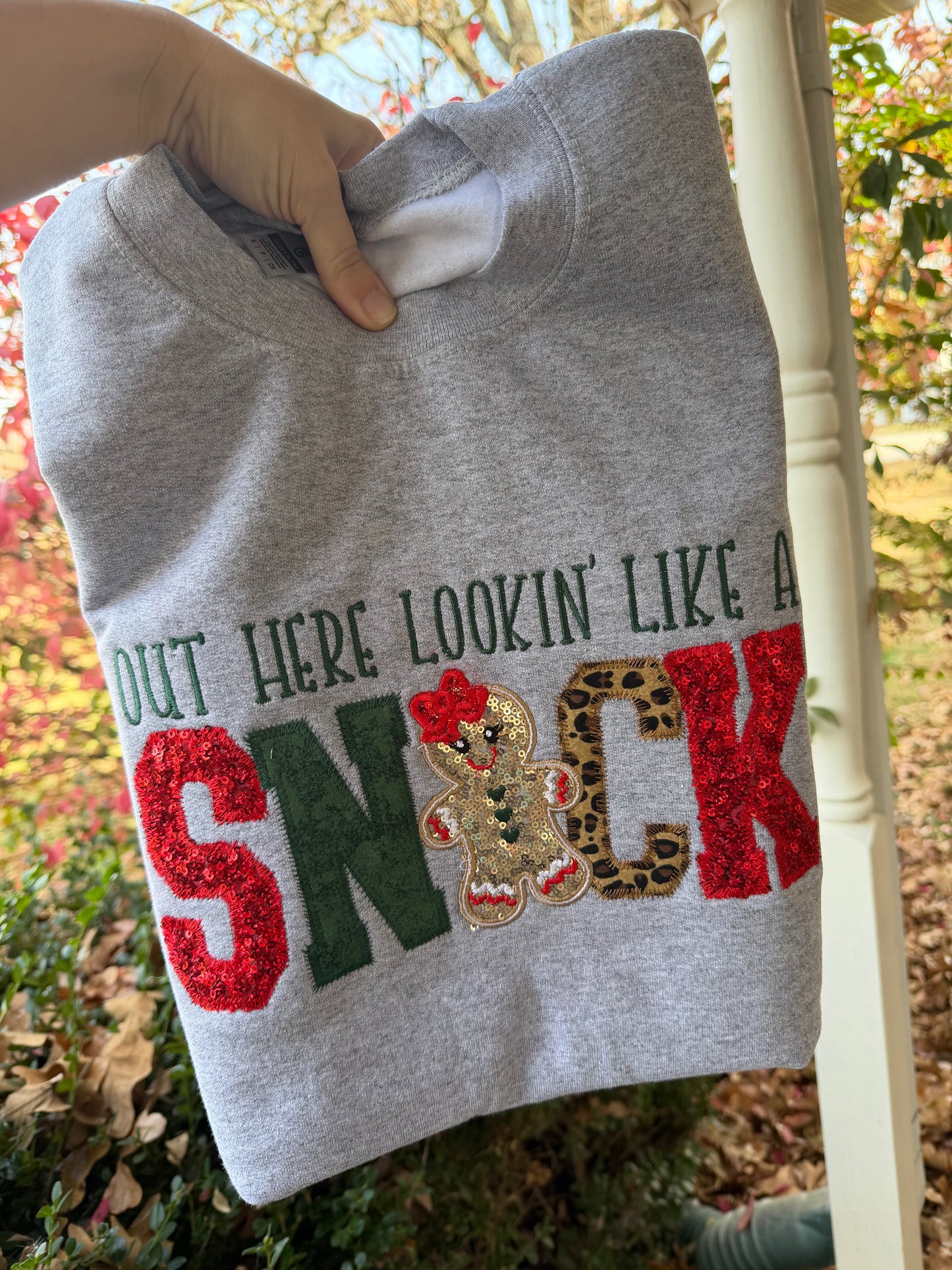 Gray sweatshirt with colorful text and gingerbread man design held outdoors.