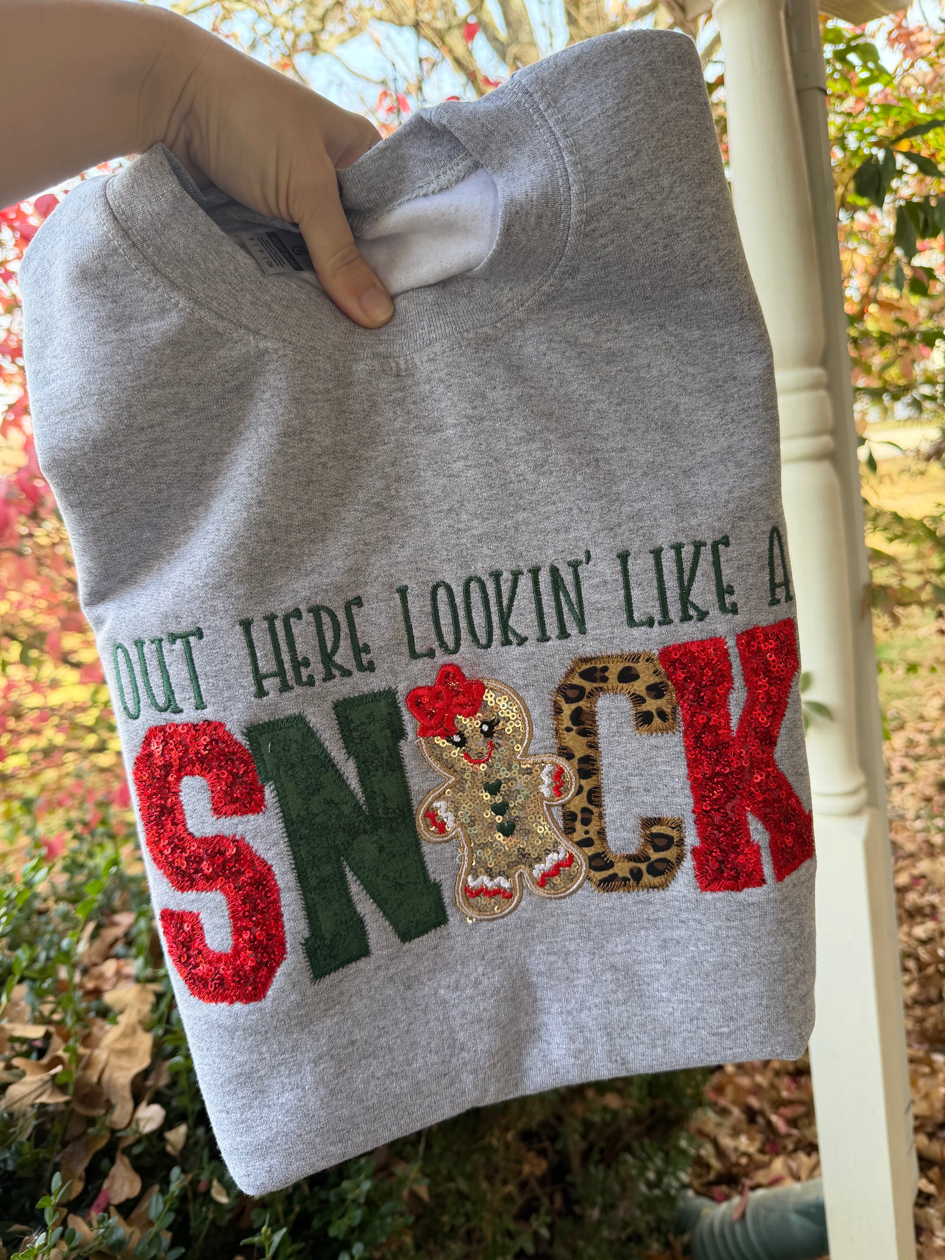 Gray sweatshirt with colorful text and gingerbread man design held outdoors.