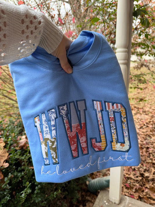 Blue sweatshirt with colorful text held by a person outdoors.