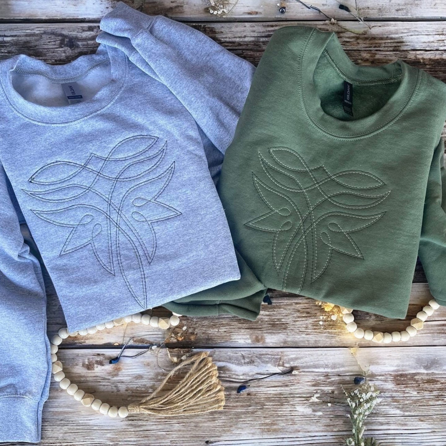 Two sweaters, one gray and one green, with leaf designs on a wooden surface.