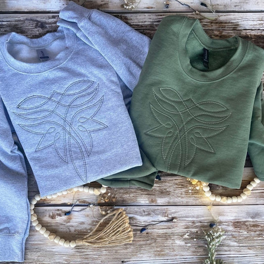 Two sweaters, one gray and one green, with leaf designs on a wooden surface.